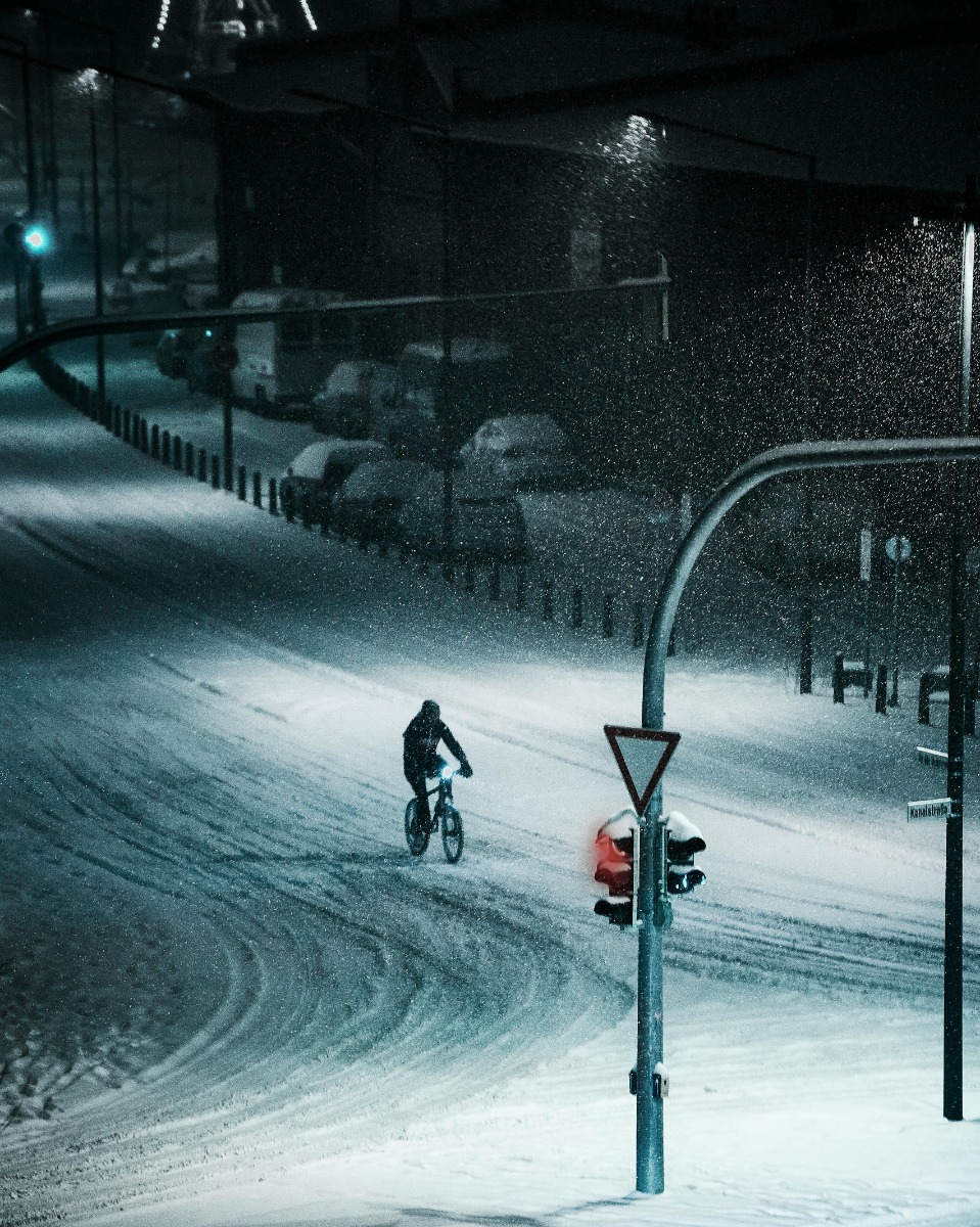 Urban evening scene with bicyclist and pedestrian amid fog and streetlights.